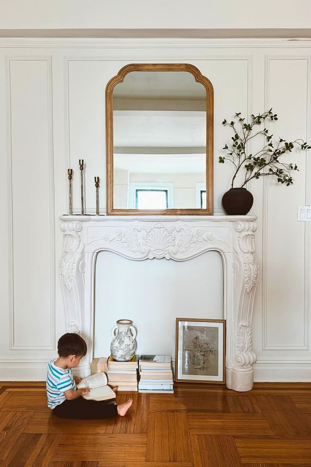 Minimalist White Fireplace Mantel with Ornate Carvings, Stacked Books, and Neutral Decor Accents in a Monochrome Living Room