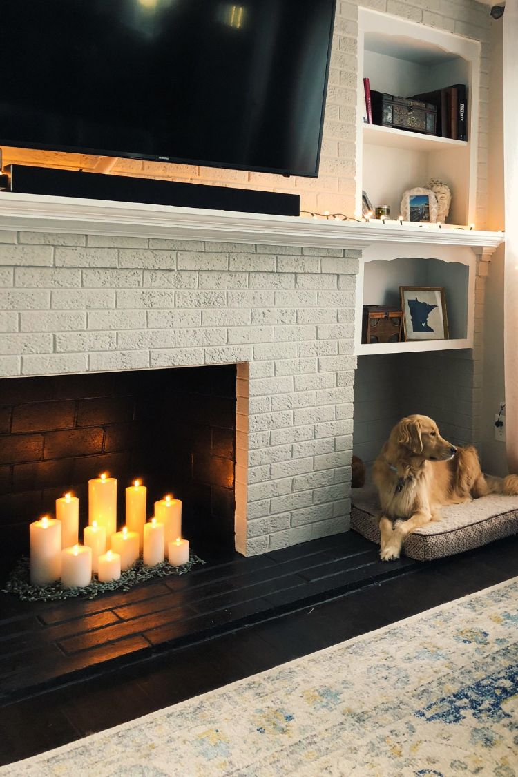 Decorative white brick fireplace with faux candles and a dog resting beside it